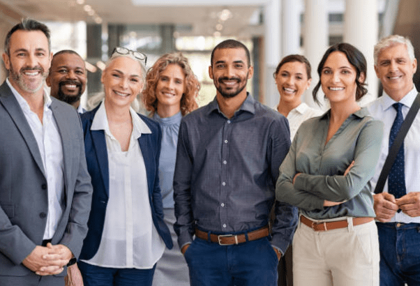 Trustack IT Services, A group of seven diverse professionals smiling and standing in a row in a bright office environment, dressed in business casual attire, inviting you to contact us.