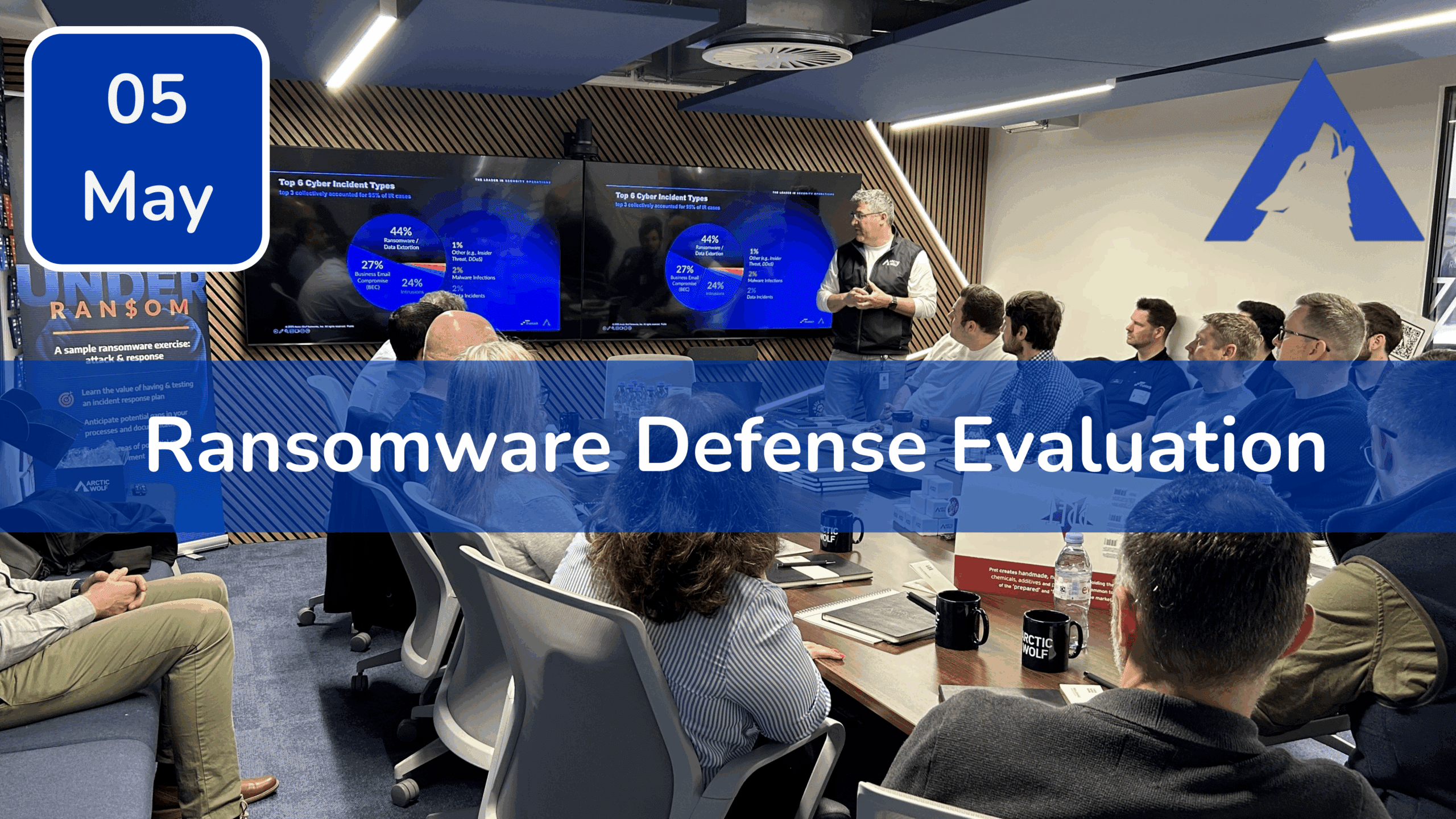 Trustack MSP Cyber Security, IT Services, IT Support. People seated in a modern conference room listen to a presenter discussing ransomware defense evaluation, with slides displayed on large screens. The date "05 May" and Trustack’s Upcoming Events to not miss are shown, plus a wolf logo in the corner.