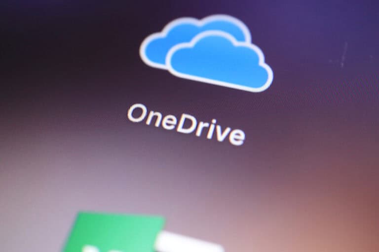 Trustack MSP Cyber Security, IT Services, IT Support. Close-up of a computer screen displaying the OneDrive logo above the text "OneDrive" on a dark background, highlighting The Importance of DLP in Business Security. A partially visible green and white icon is at the bottom left.