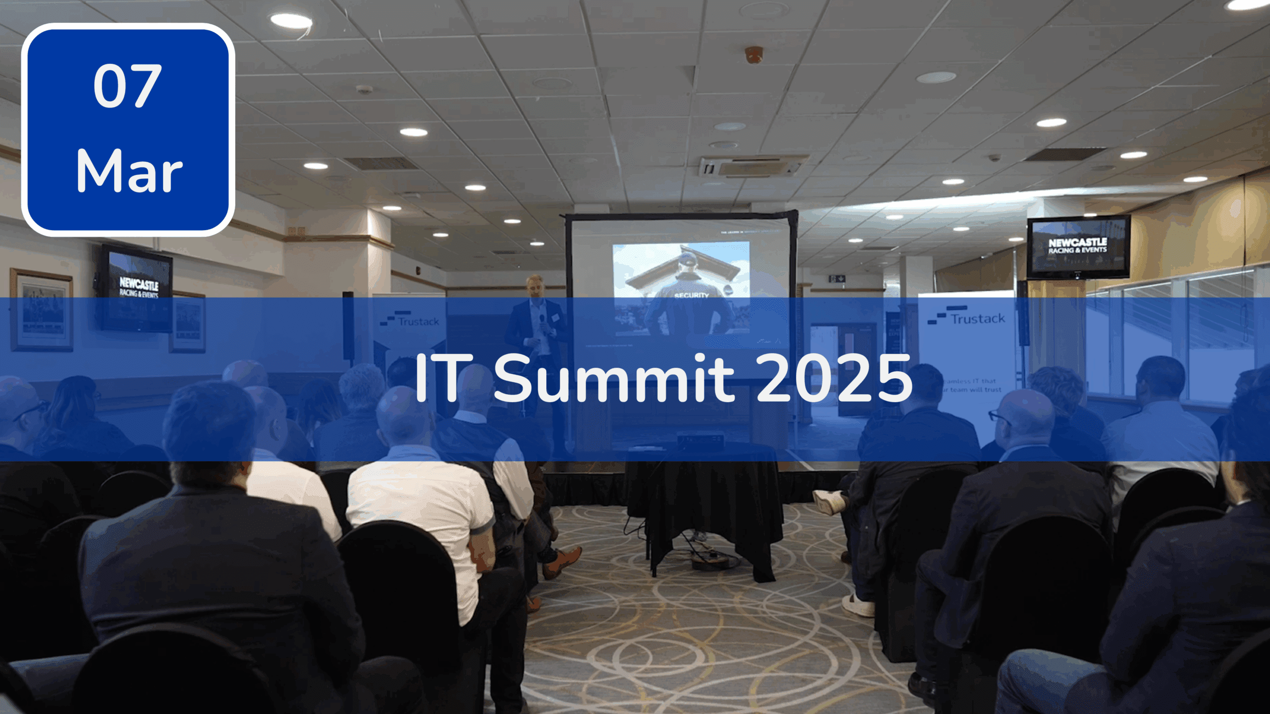 Trustack MSP Cyber Security, IT Services, IT Support. A group of people is seated in a conference room facing a speaker and a projector screen. Text overlay reads "IT Summit 2025" with a blue box showing "07 Mar" in the corner—one of Trustack's Upcoming Events to not miss.