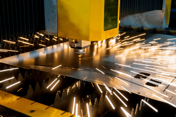 Trustack MSP Cyber Security, IT Services, IT Support. A CNC laser cutting machine slices through a sheet of metal in an industrial manufacturing setting, producing bright sparks around the cutting area.