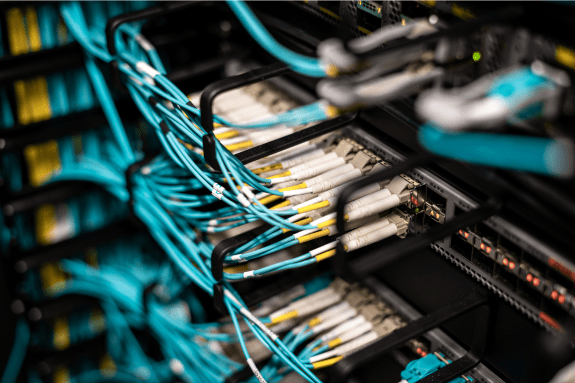 Trustack MSP Cyber Security, IT Services, IT Support. A close-up view of network servers connected by numerous turquoise Ethernet cables, showing detailed ports and wiring in a data centre environment designed for secure, immutable backups.