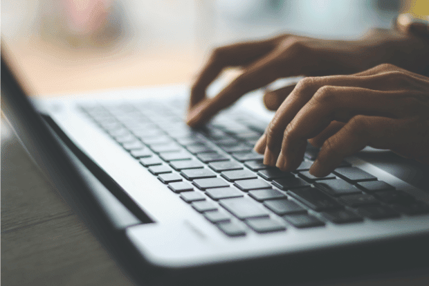 Trustack MSP Cyber Security, IT Services, IT Support. Close-up of a person's hands typing on a laptop keyboard, with light reflecting off the keys. The background is blurred, highlighting focused Virtual Desktop Access and activity on the keyboard.