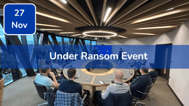 Trustack MSP Cyber Security, IT Services, IT Support. A group of people sit around a circular conference table in a modern meeting room with large windows. Text over the image reads "Under Ransom Event" and "27 Nov" in a blue box—one of Trustack's Upcoming Events not to miss.