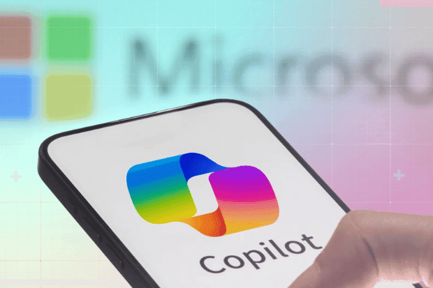 Trustack MSP Cyber Security, IT Services, IT Support. A smartphone screen displays the Microsoft Copilot logo and name. In the blurred background, part of the Microsoft logo is visible as a finger interacts with the phone, highlighting Microsoft Copilot in action.