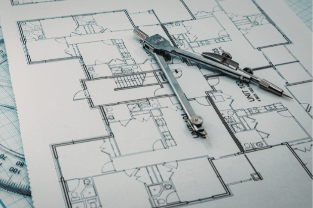 Trustack MSP Cyber Security, IT Services, IT Support. A pair of compasses rests on a detailed architectural floor plan, showing various rooms and unit numbers. A transparent ruler with measurement markings highlights the precision required in architecture.