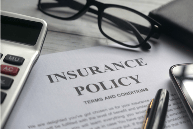 Trustack MSP Cyber Security, IT Services, IT Support. A close-up of an insurance policy document on a desk with a calculator, spectacles, pen, and wallet placed nearby. The words "INSURANCE POLICY" are prominently displayed on the paper.