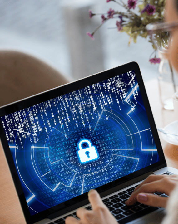Trustack MSP Cyber Security, IT Services, IT Support. A person types on a laptop displaying a blue digital lock icon, symbolising the importance of DLP in business security amid supply chain risk. Binary code and abstract graphics highlight data protection, while a vase with flowers is blurred in the background.