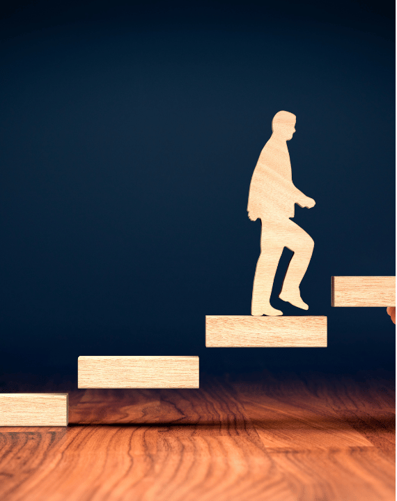Trustack MSP Cyber Security, IT Services, IT Support. A wooden silhouette of a person is shown climbing upward on a staircase made of wooden blocks, symbolising overcoming supply chain risk, with a dark blue background and a wooden surface below.